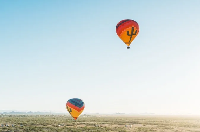 Two balloons rising in a clear morning sky above the desert