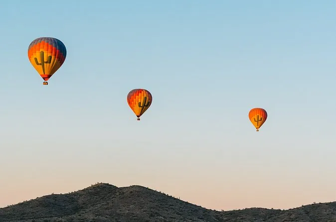 Three hot air balloons drifting over desert hills at sunrise